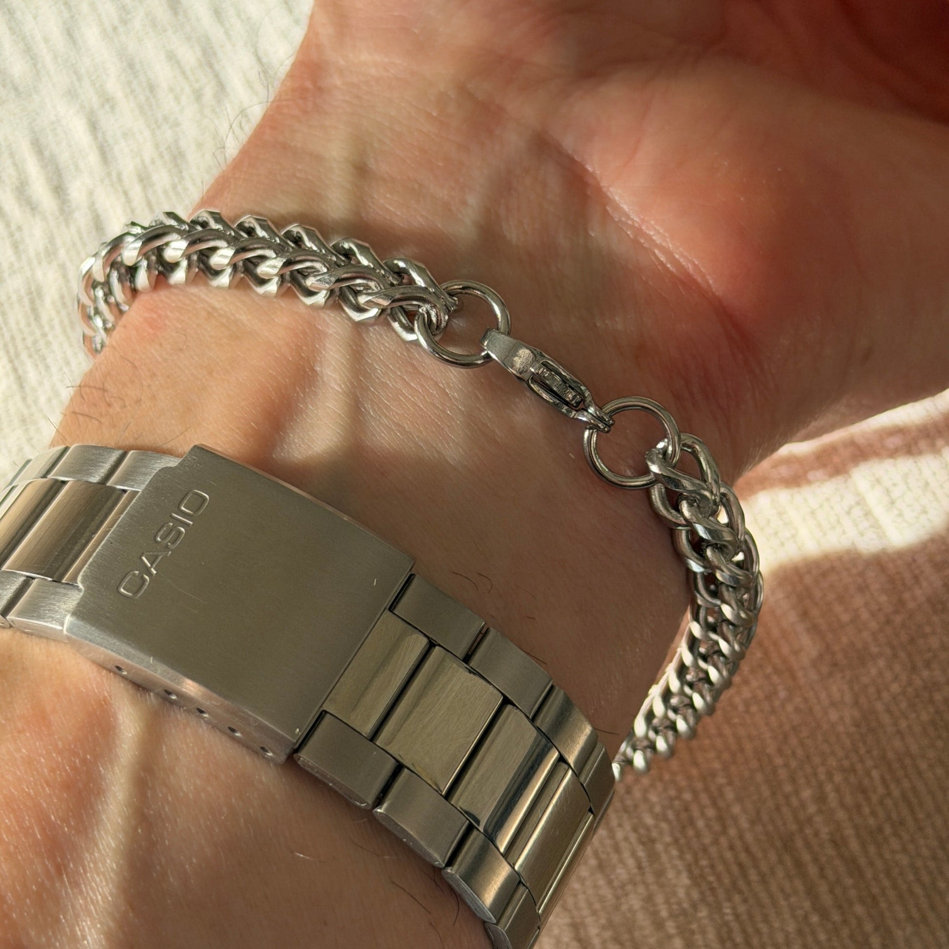 Hand wearing a silver bracelet on a neutral background