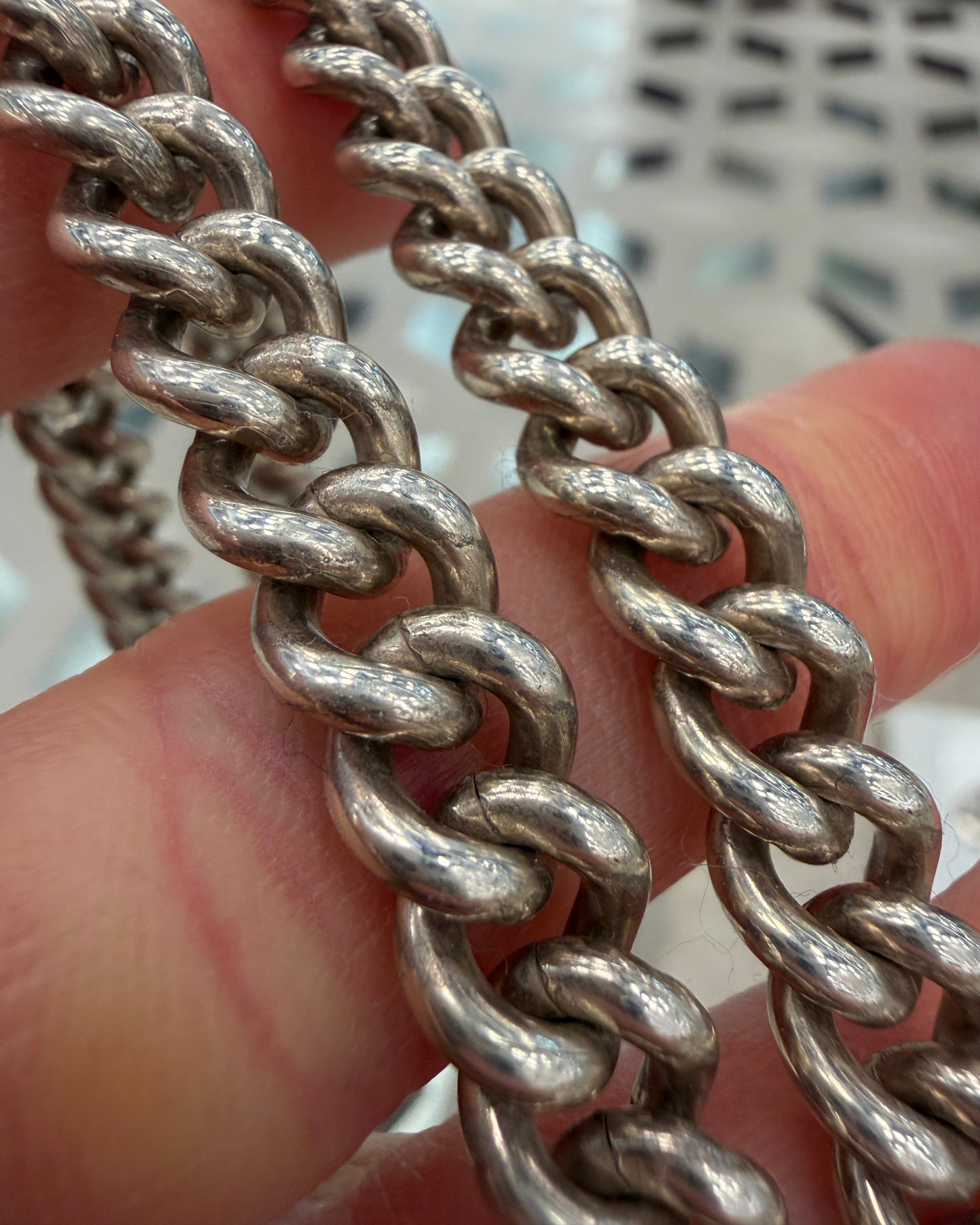 Close-up of a silver chain held between fingers with a blurred background